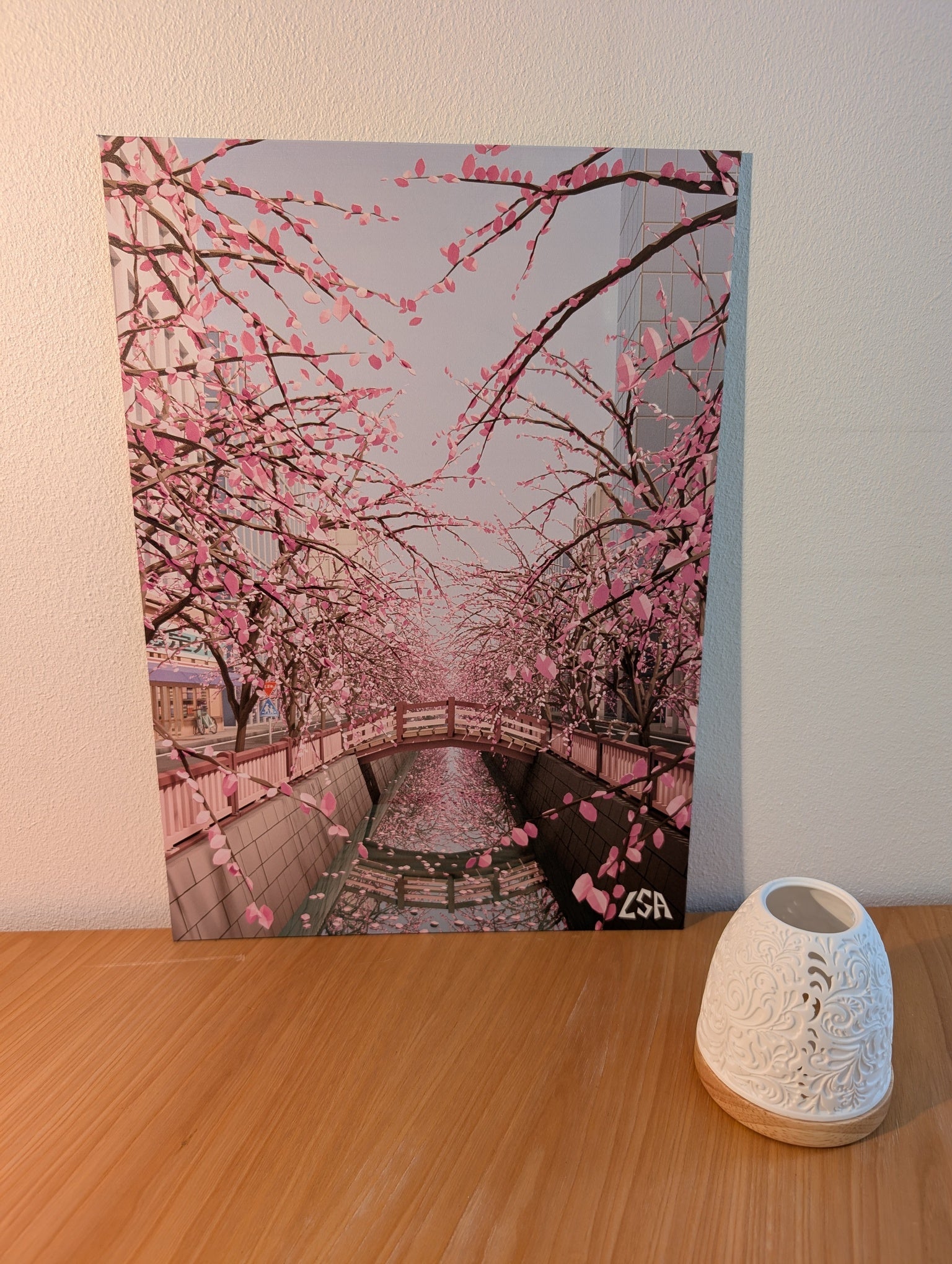 Aluminium print depicting a canal in tokyo lined with blooming pink cherry blossom trees, with a small bridge and buildings in the background in low-poly stye