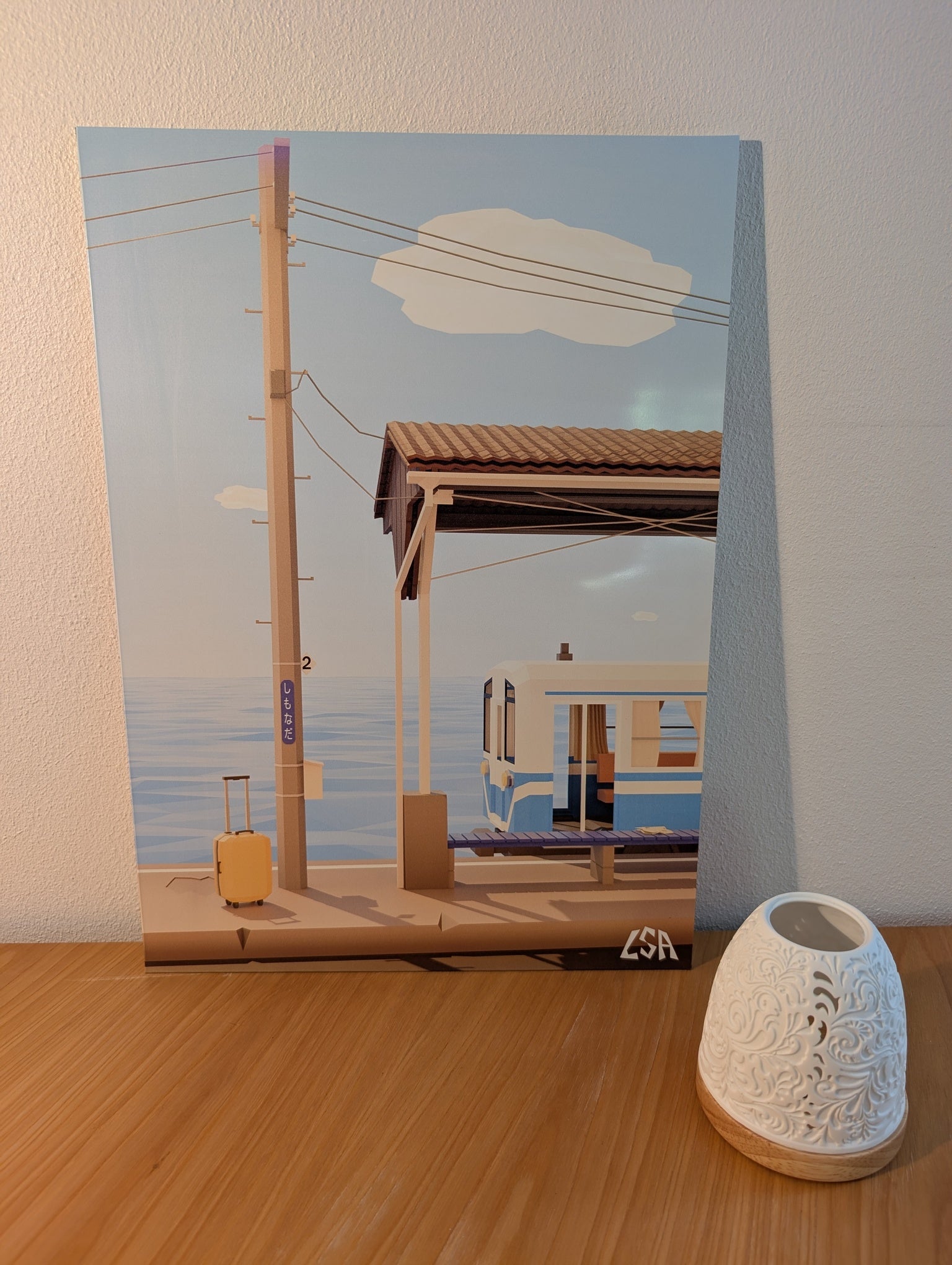 A low-poly stylized aluminium print featuring a train station platform with a blue ocean in the background, a train, a utility pole, a suitcase, and a small cloud in the sky