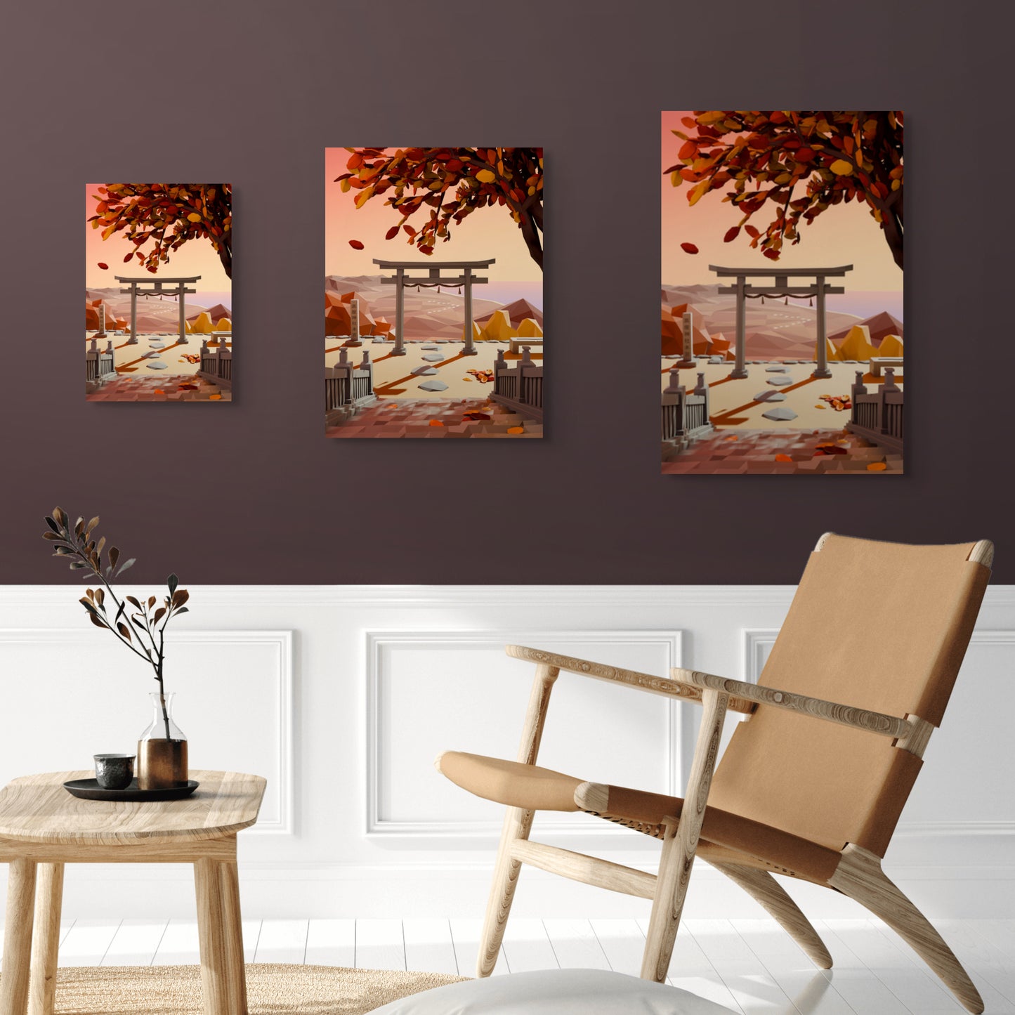 Three low poly style artworks of a Japanese torii gate scene with an autumn sunset with view on mountains and sea displayed on a wall with a beige chair and small table below. 