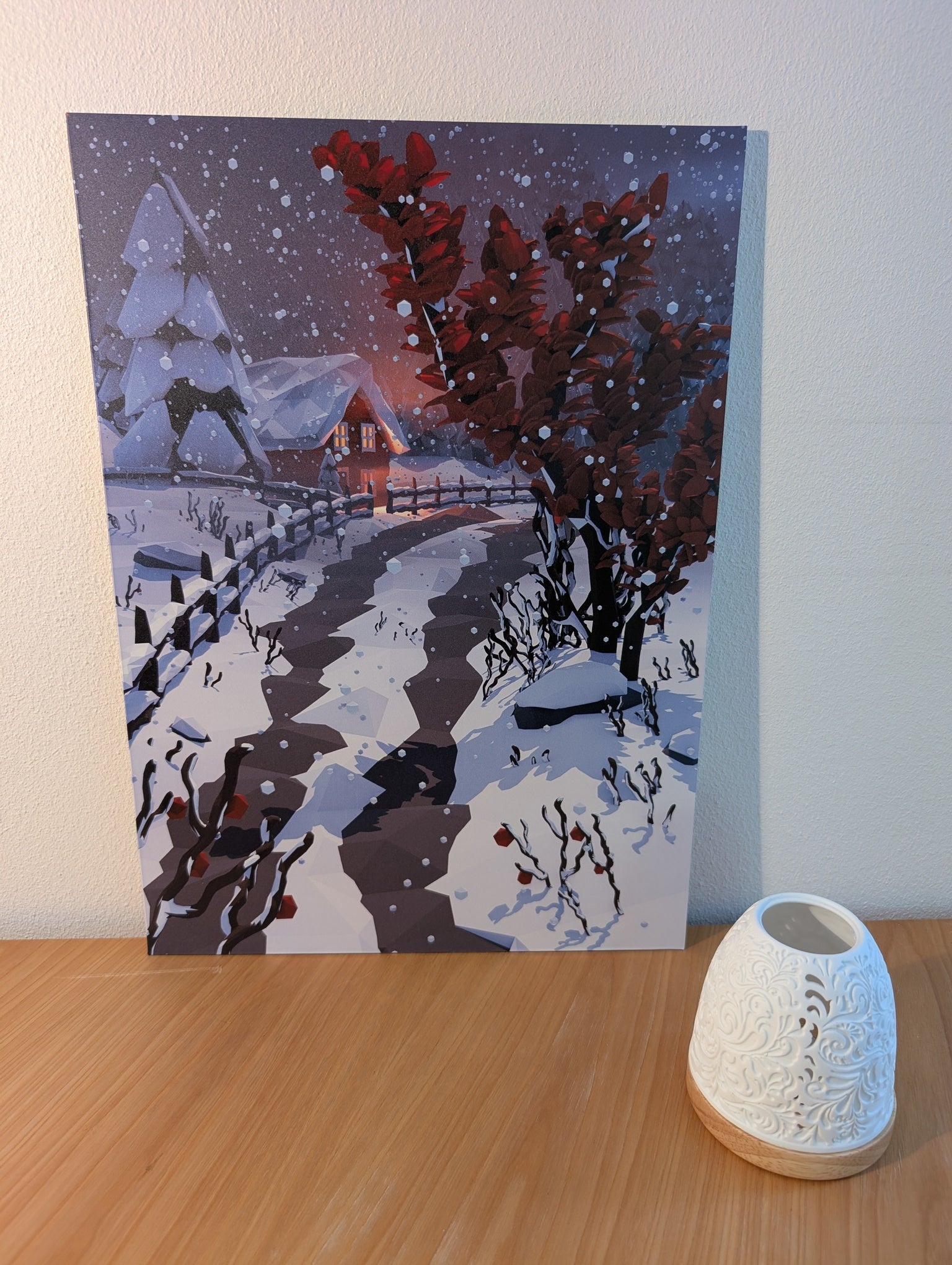 Aluminium print featuring a snow-covered path leading to a warmly lit house, with snow-laden trees and a dark red leafy bush in the foreground under a snowy night sky.